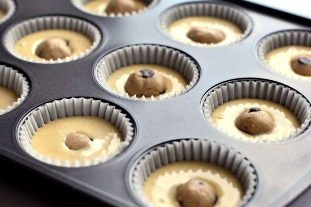 Muffin tins with liners, cupcake batter, and cookie dough in the center - unbaked