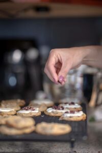 Person sprinkling cranberries on top of frosted cookies