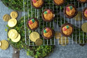 Pot of Gold Cookie Cups on cooling rack over four-leaf clover decorative cooling pad and surrounded by gold coins