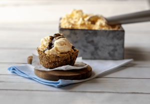 Chocolate Chip Cookie Ice Cream bowl filled with vanilla ice cream and topped with fudge next to box of ice cream with scoop.