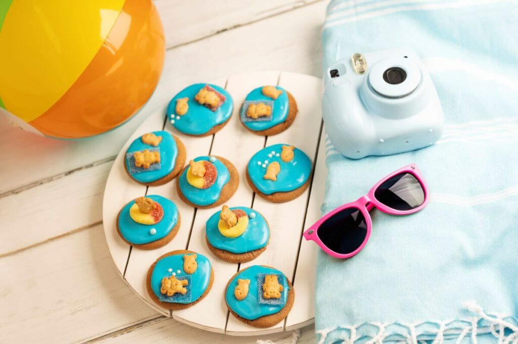 A series of Summer Beach Cookies on a plate with a beach towel, beach ball, camera, and glasses as decor