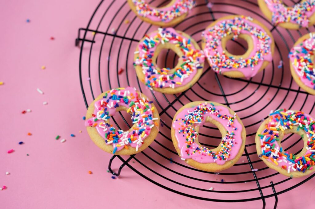 Several Confetti Donut Cookies on a cooling rack with sprinkles all around.