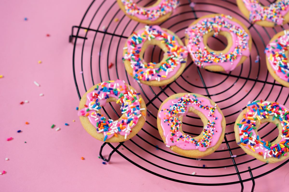 Several Confetti Donut Cookies on a cooling rack with sprinkles all around.
