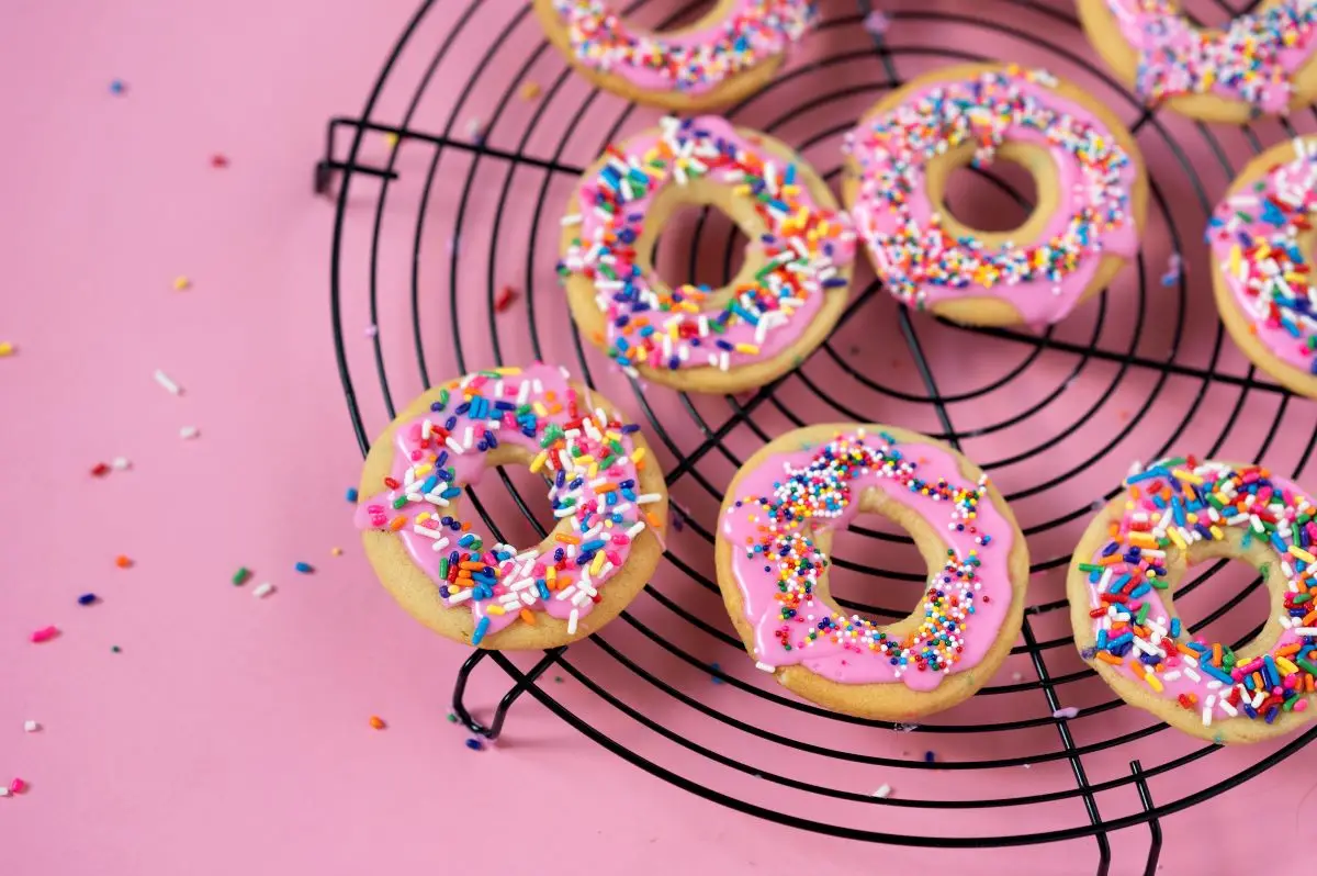Several Confetti Donut Cookies on a cooling rack with sprinkles all around.
