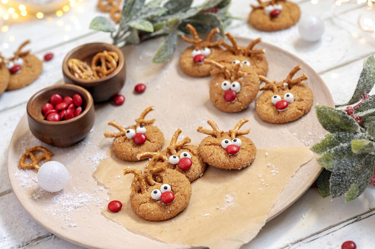 Tray of Rudolph Peanut Butter Cookies with red chocolate candies and pretzels in bowls next to the cookies.