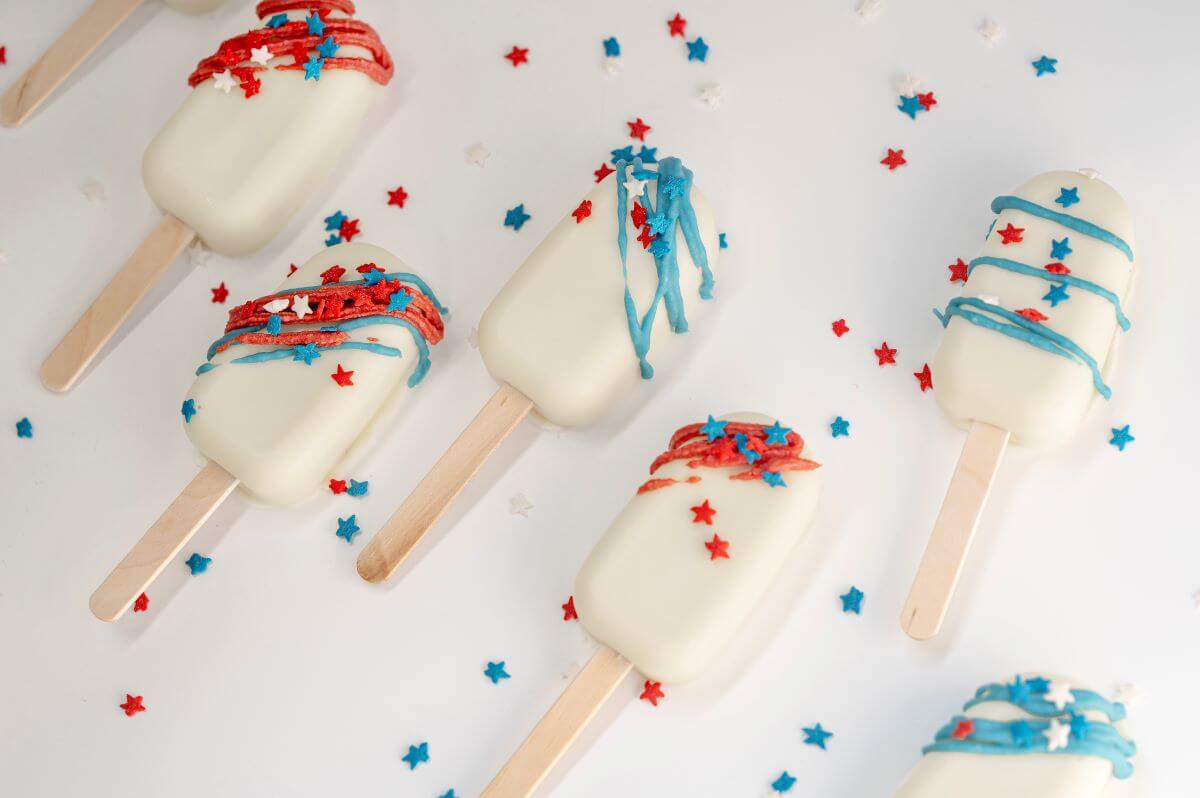 Red, White, and Blue Cookiesicles on a white background with colored star sprinkles scattered around them.