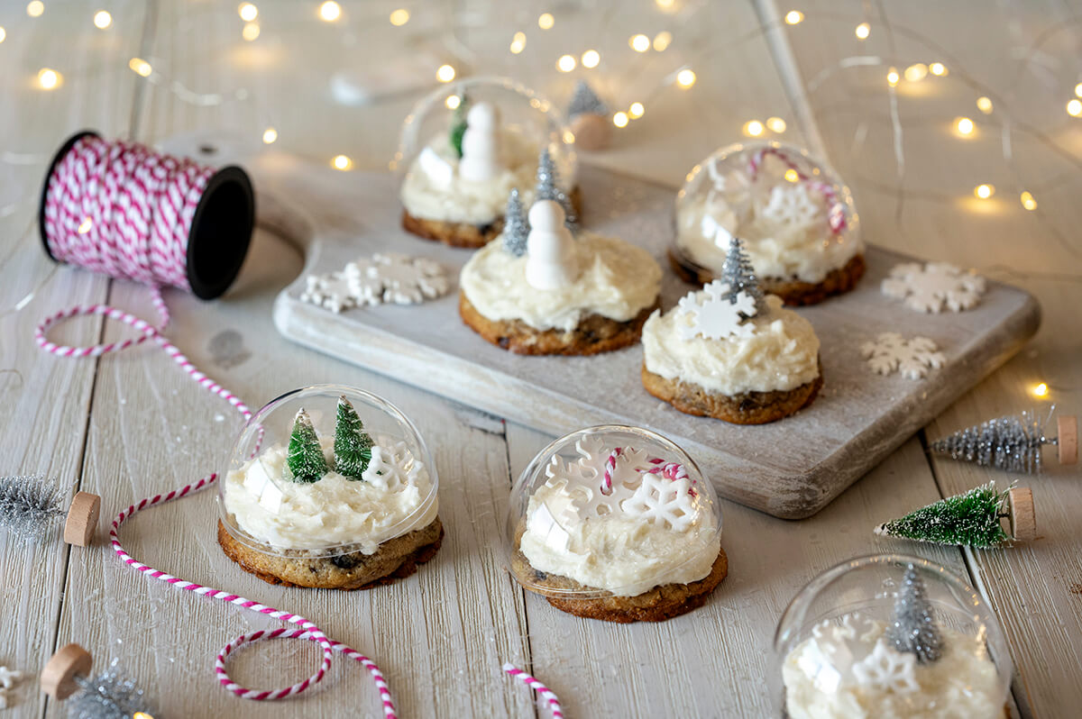 Snow Globe Cookies on a wood surface, surrounded by lights, string, and other decorations.