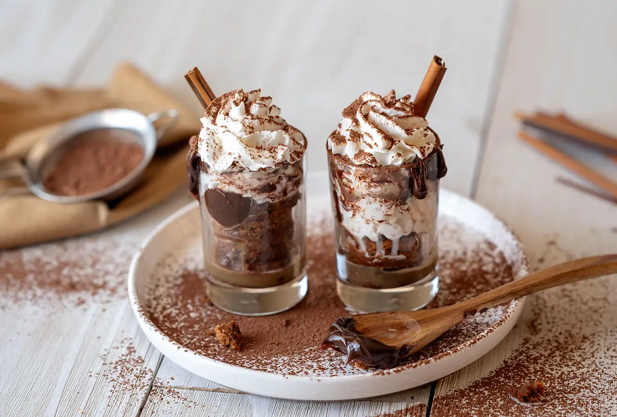 Two Peanut Butter Sundaes with homemade caramel sauce and hot fudge on a plate dusted with cocoa powder.