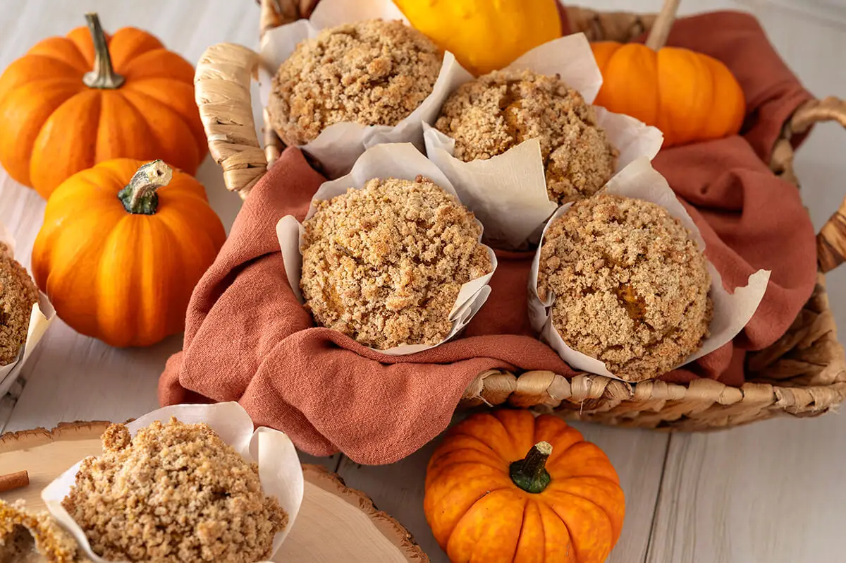 Chocolate Chip Cookie Dough Pumpkin Muffins in a basket and on a serving platter. They are surrounded by fall decor.